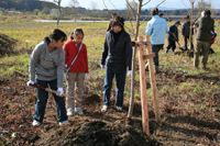 ２０団体・家族がそれぞれの思いを込めて記念の桜を植樹しました。（９日、米代川河川公園で）2